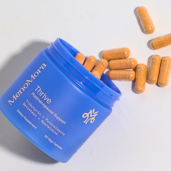 Blue container of MenoMora Thrive supplements with orange capsules on a light gray background
